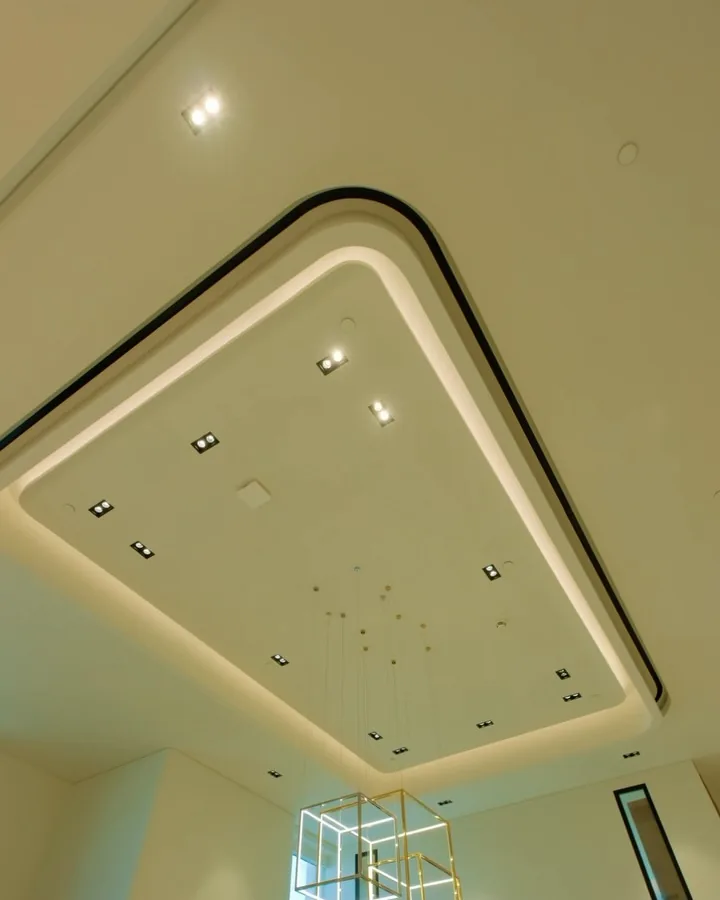 A curved gypsum ceiling with a warm cove light, recessed downlights and a linear AC slot in a villa finished by Oryx Design