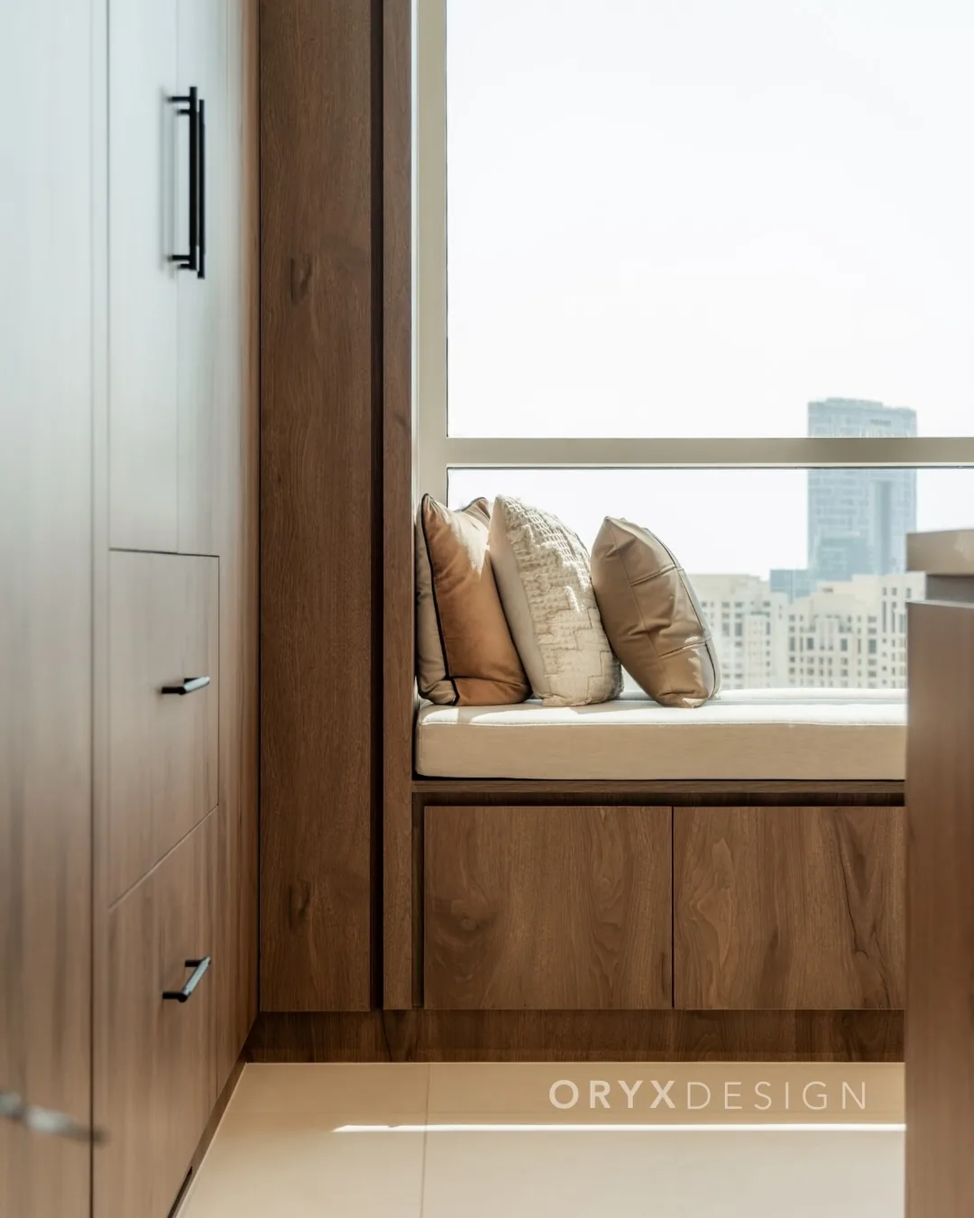 A built-in timber window seat with cushions and full-height fitted wardrobes by Oryx Design, overlooking the Dubai skyline