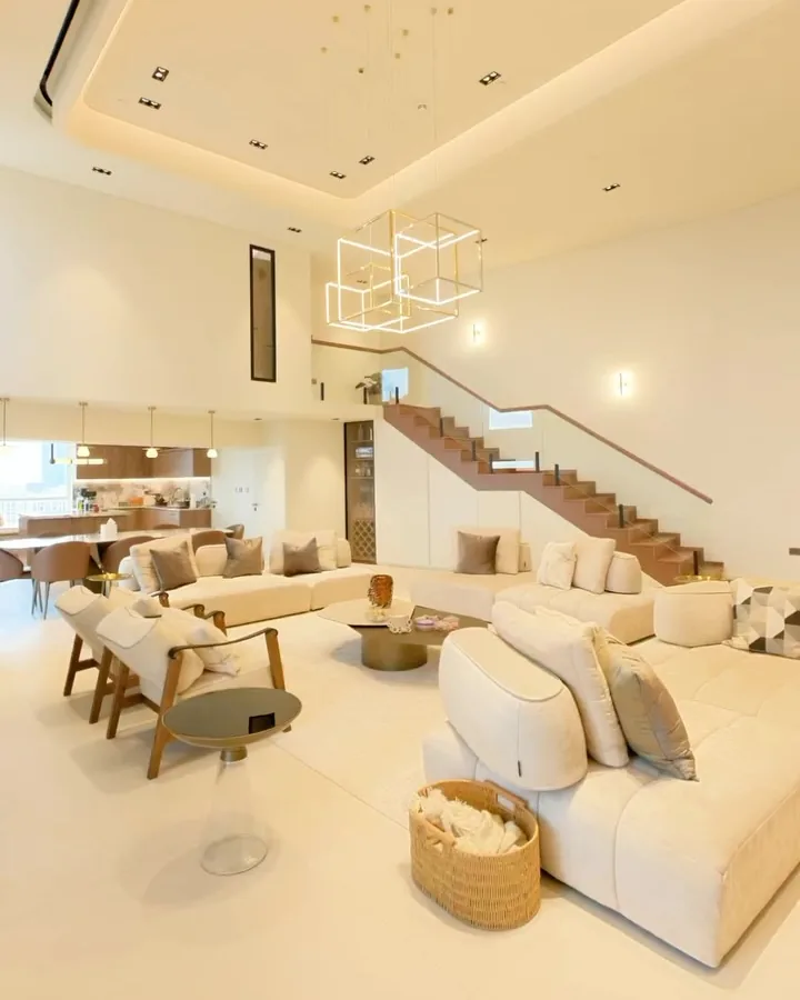 The double-height living room of the Sadaf 8 villa by Oryx Design, cream sofas, a floating staircase and one warm material palette running through the space
